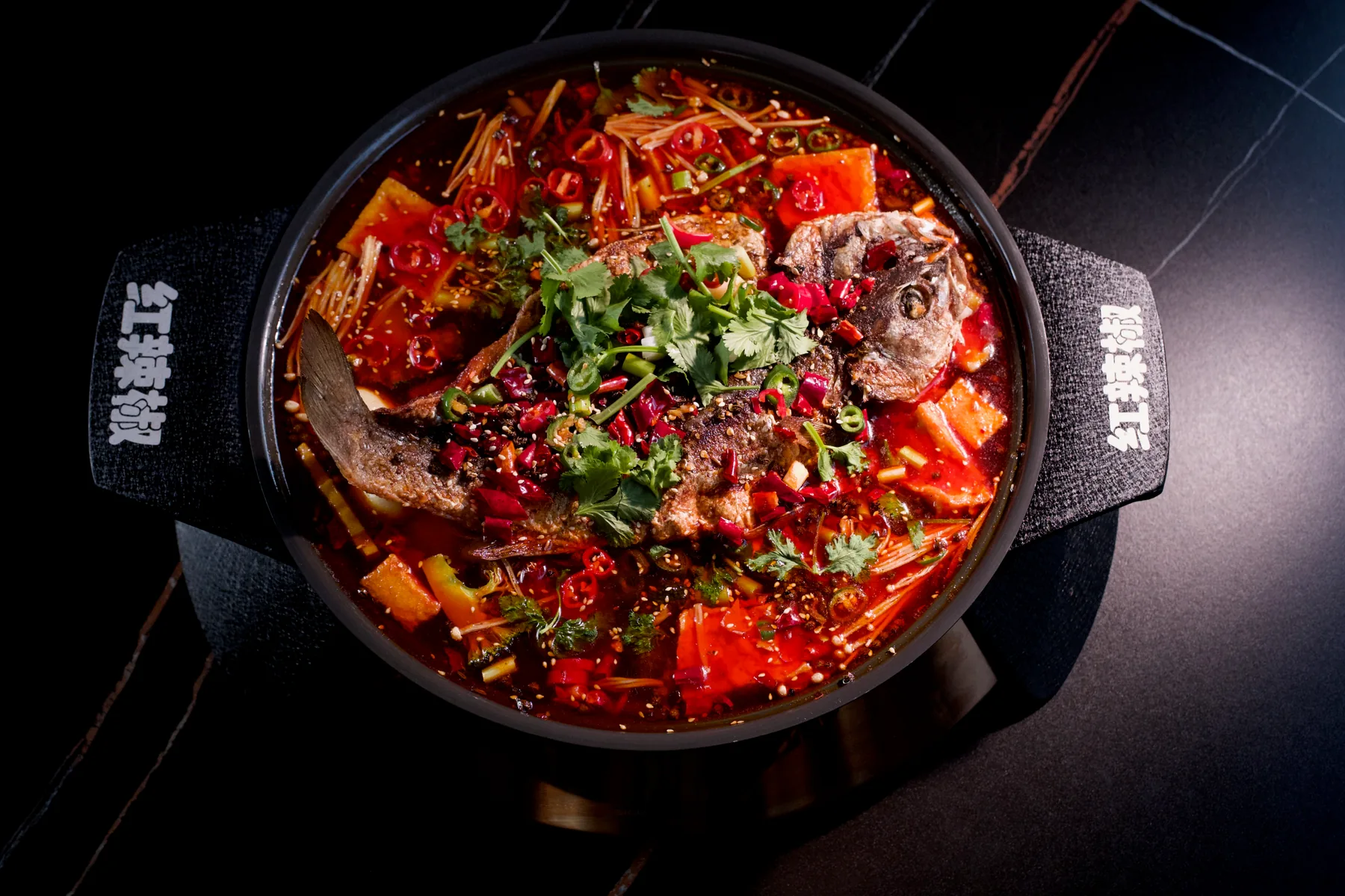 The finished sea bass in a deep pot of scarlet chilli broth under coriander and sliced peppers