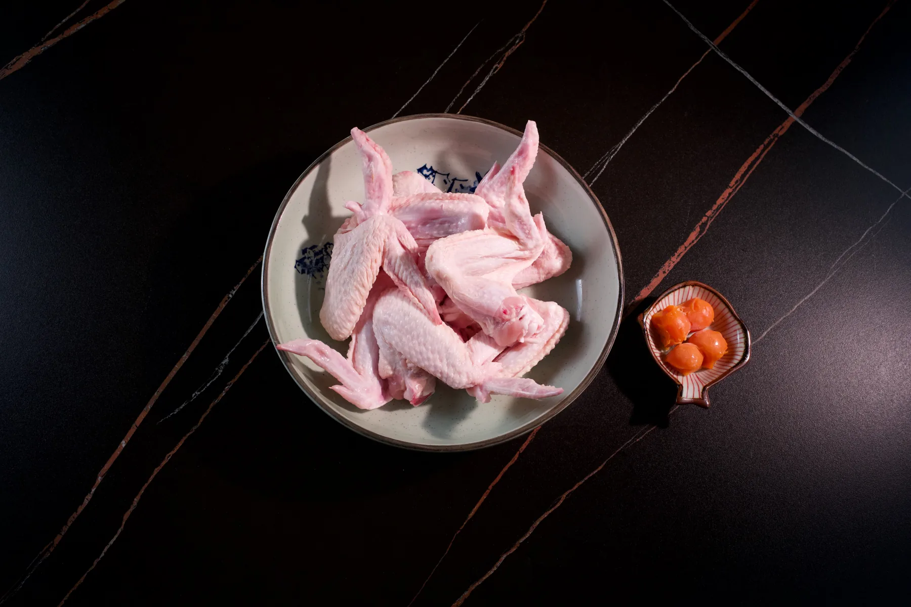 Raw chicken wings in a shallow white bowl on a dark marble counter