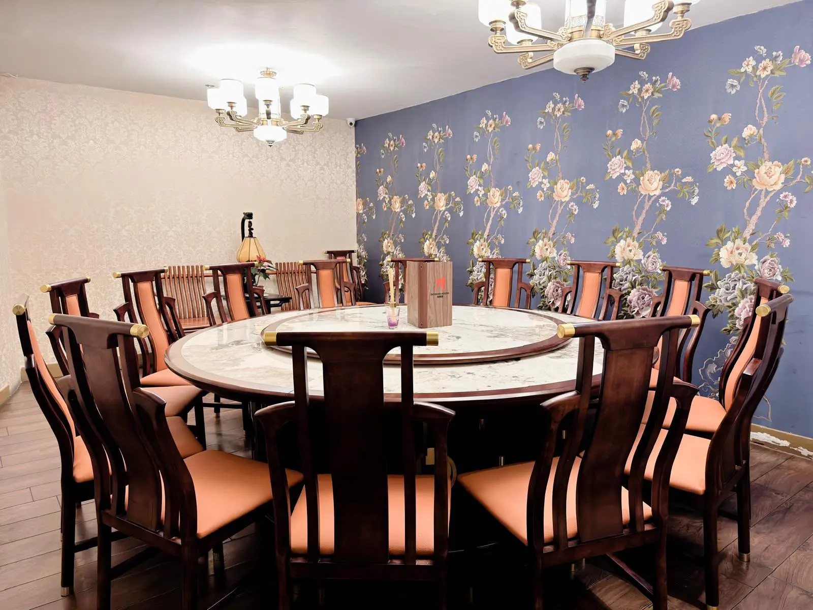 The Function Room: a big round marble table with a lazy Susan, ringed by wooden chairs, under two chandeliers beside a floral wallpaper wall